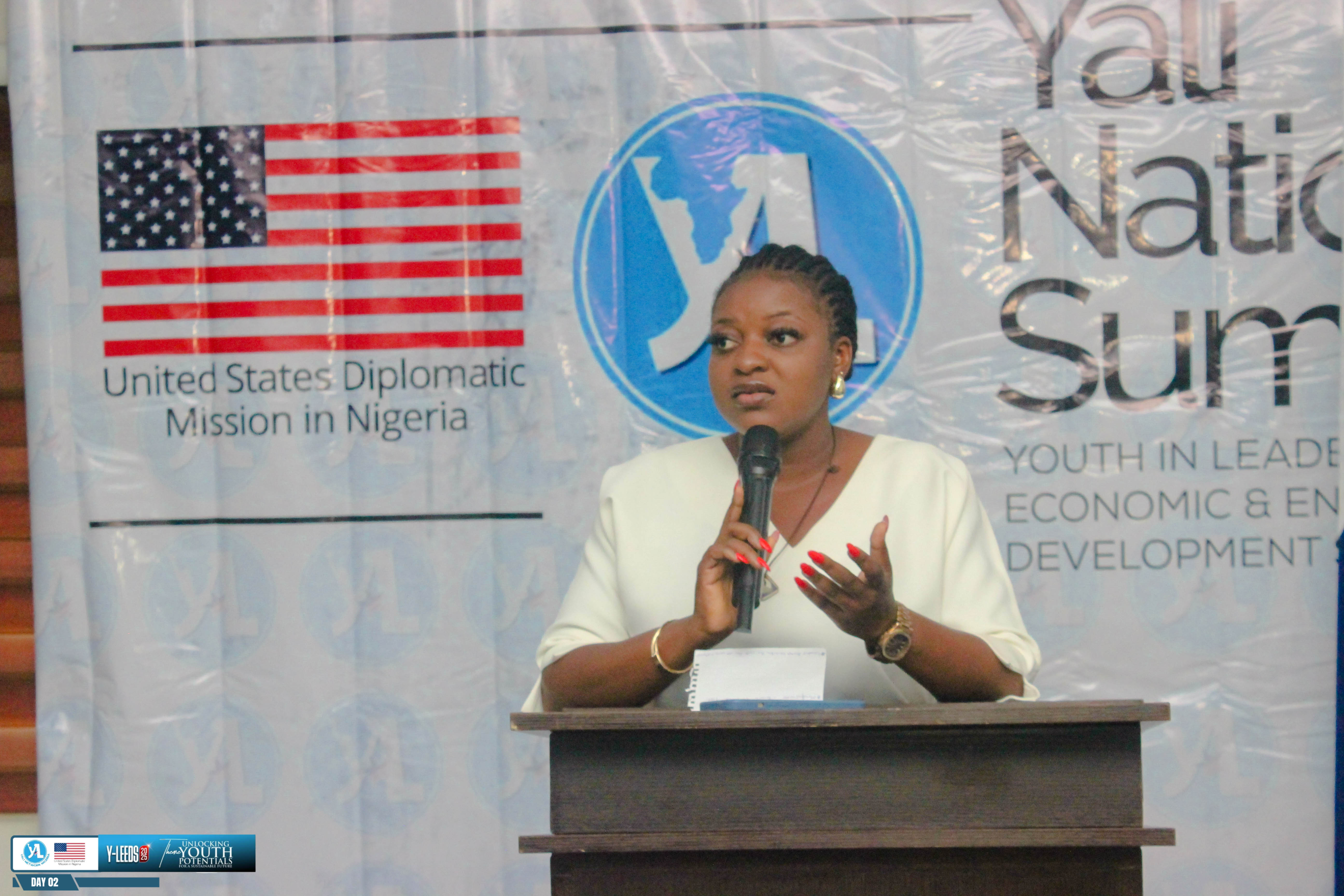 A YALI Network Nigeria speaker at the podium, backed by the United States Diplomatic Mission in Nigeria banner, at Y-LEEDS 2025